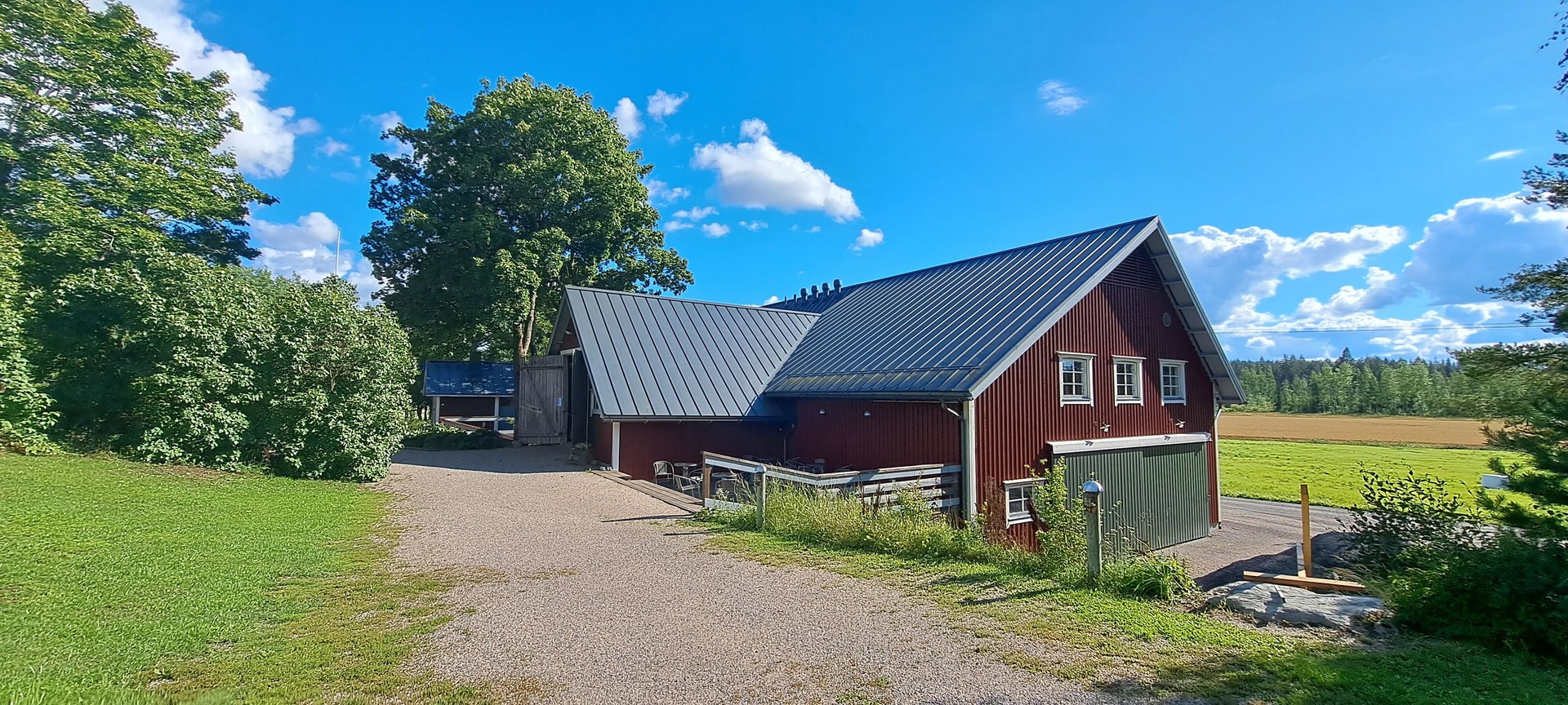 Kuvassa KulttuuriNavetta ulkoapäin. Rakennus on rakennettu rinteeseen. Se on punamullan värinen ja siinä on tumma peltikatto. Käynti tilaan on vanhan ylisin kohdalta leveistä ovista rinteen yläosasta.